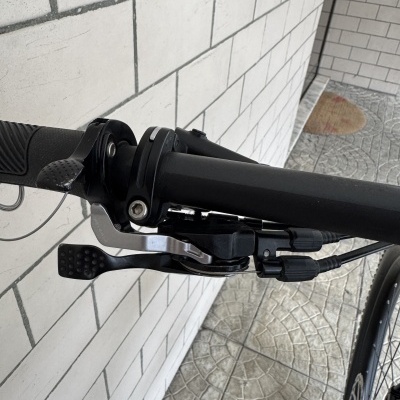Guiador preto de bicicleta com punho de borracha e alavanca de travão junto a parede de azulejos brancos.