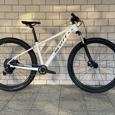 Bicicleta de montanha SCOTT branca com suspensão preta encostada em parede de azulejos brancos