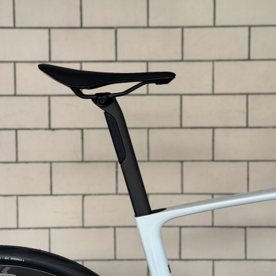 Assento de bicicleta preto com tija de assento preta e quadro branco junto a uma parede de azulejos creme