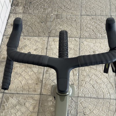 Guiador de bicicleta preto com pneu dianteiro visto de cima sobre pavimento azulejado cinzento