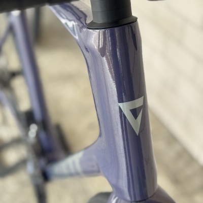 Detalhe do quadro azul de uma bicicleta com adesivo branco e garfo preto