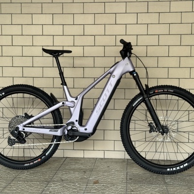 Bicicleta de montanha elétrica cinzenta com pneus Maxxis encostada numa parede de azulejos