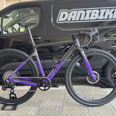 Bicicleta de estrada cinza e roxo com pneus de borracha preta e guiador envolvido em fita preta, em frente a carrinha preta com texto DANIBIKES