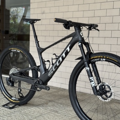 Bicicleta de montanha Scott preta com suspensão FOX e pneus Pirelli Scorpion encostada numa parede de tijolos