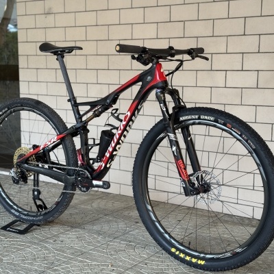 Bicicleta de montanha Specialized S-Works com quadro vermelho e preto encostada contra parede