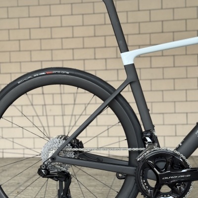 Bicicleta de estrada preto e branco com componentes Dura-Ace junto a parede de tijolos.