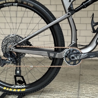 Parte traseira de bicicleta cinza com roda preta, corrente dourada e pedaleira GX SR