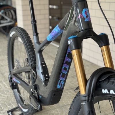 Bicicleta de montanha elétrica SCOTT com quadro cinza escuro e detalhes em azul e roxo.