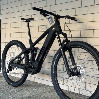 Bicicleta de montanha preta com suspensão dianteira e traseira encostada numa parede de azulejos brancos