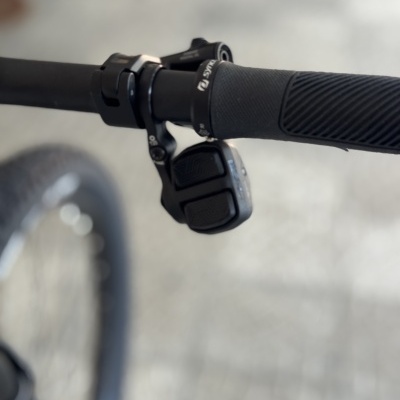 Punho de bicicleta preto com alavanca de mudança e roda ao fundo