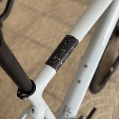 Parte de um quadro de bicicleta branca com detalhe preto e pontos brancos, assento e rodas pretas, chão pavimentado