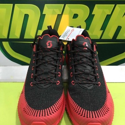 Sapatilhas desportivas preto e vermelho com etiqueta numa superfície verde