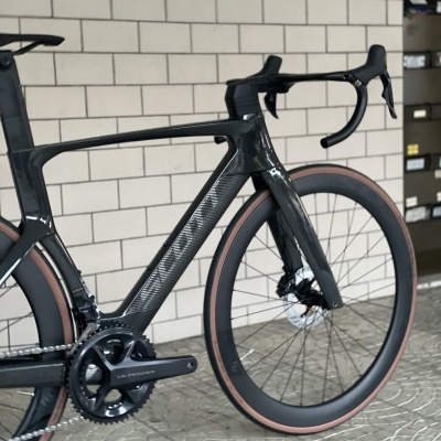 Bicicleta de estrada negra com pneus marrons e guiador drop em ambiente interior