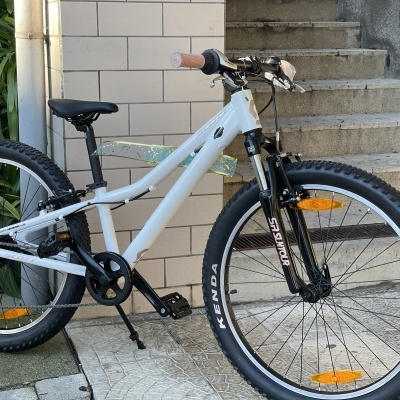 Bicicleta branca para crianças com pneus pretos e detalhes em rosa junto a parede e escadas de cimento