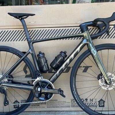 Bicicleta de estrada Scott preta e verde com garrafas pretas encostada a caixa de cartão