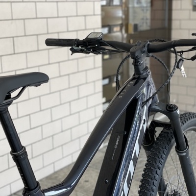 Bicicleta elétrica preta com pneus de cravos junto a uma parede de azulejos brancos