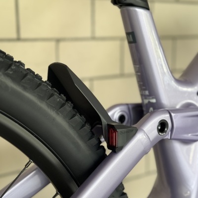 Detalhe traseiro de bicicleta lilás com pneu preto e guarda-lamas com reflector