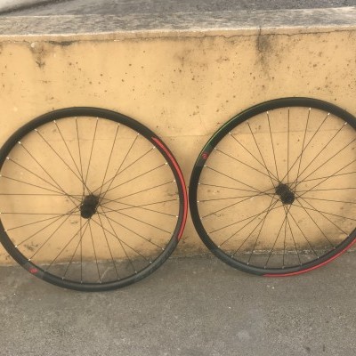 Duas rodas de bicicleta com aro preto e detalhes vermelhos encostadas a uma parede amarela