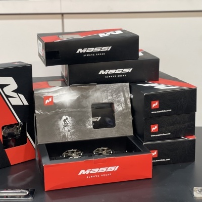 Caixas de embalagem de produtos MASSI em preto, vermelho e branco com peças metálicas visíveis