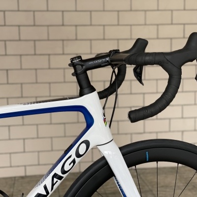 Bicicleta de estrada branca e azul com guiador preto encostada a parede de tijolos