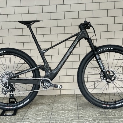 Bicicleta de montanha preta com suspensão dianteira contra uma parede de azulejos brancos