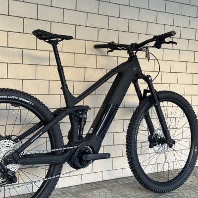 Bicicleta de montanha elétrica preta encostada numa parede de azulejos brancos.