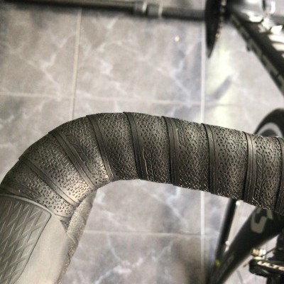 Guiador de bicicleta com fita preta texturada e quadro preto sobre chão de azulejos cinzentos