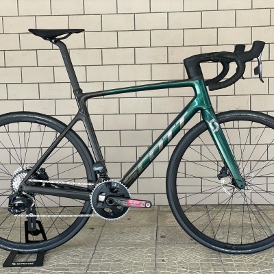 Bicicleta de estrada verde e preta encostada a uma parede branca