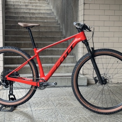 Bicicleta de montanha vermelha com pneus castanhos e componentes pretos junto a escadas