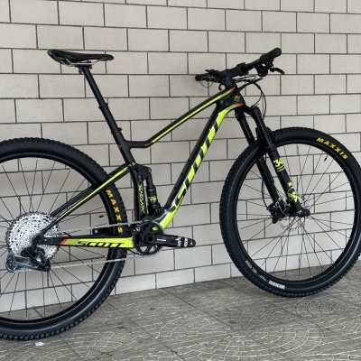 Bicicleta de montanha SCOTT preto e amarelo com pneus MAXXIS junto a parede branca