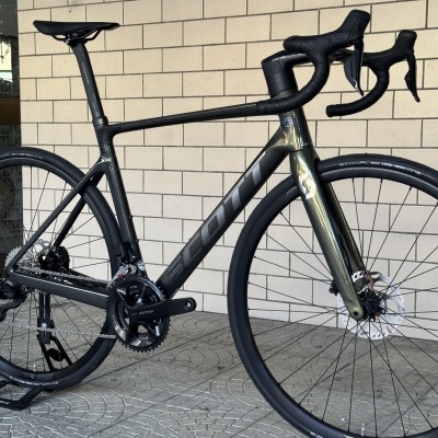 Bicicleta de estrada preta com componentes Shimano 105, quadro em carbono com texto SCOTT e pneus Schwalbe One