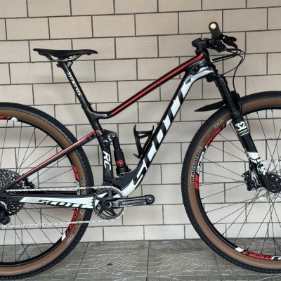 Bicicleta de montanha Scott preta, branca e vermelha encostada numa parede de azulejos brancos.