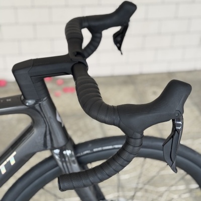 Guidão preto de bicicleta de estrada com fitas e manetes, roda aerodinâmica e fundo de tijoleira e azulejos brancos