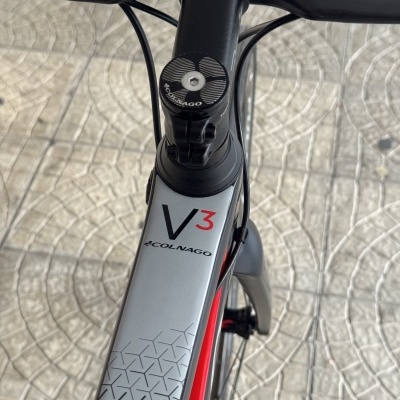 Bicicleta preta, cinza e vermelha com marca COLNAGO e modelo V3, vista de cima focada no guiador e tubo superior.