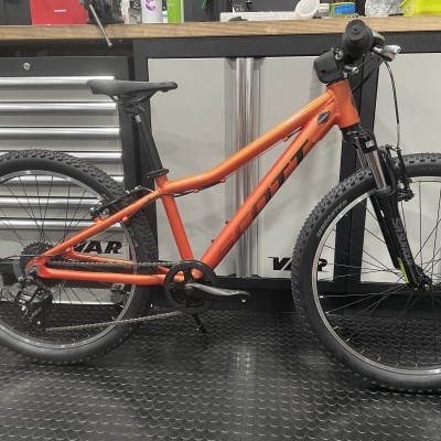 Bicicleta de montanha alaranjada numa oficina com ferramentas e armários ao fundo