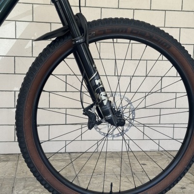 Roda dianteira de bicicleta com suspensão e pneu preto junto a parede de tijolos brancos