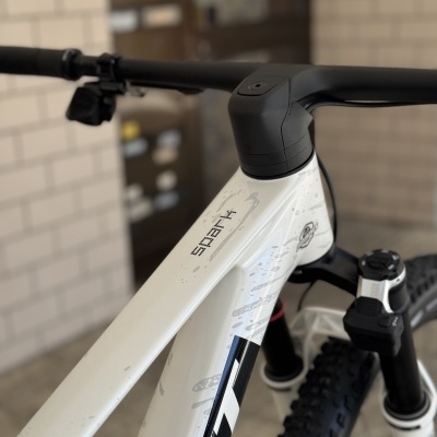 Bicicleta de montanha branca com nome SPARK no quadro e guiador preto num ambiente interior