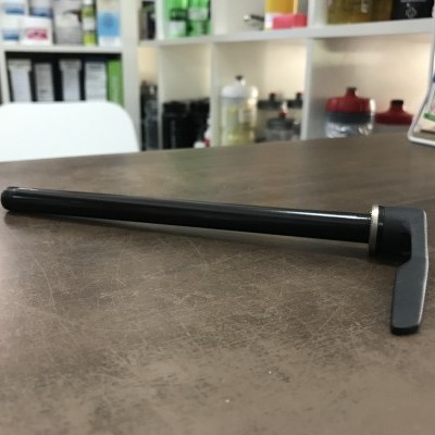 Ferramenta preta com cabo longo e cabeça metálica sobre mesa marrom com prateleiras ao fundo