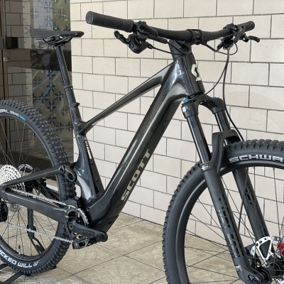 Bicicleta elétrica preta com suspensão dianteira e pneus Schwalbe junto a parede de tijolos.