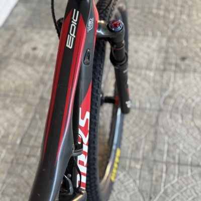 Bicicleta de montanha preta e vermelha com texto EPIC e S WORKS, pneus Maxxis e suspensão dianteira ajustável