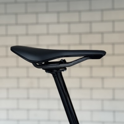 Selim de bicicleta preto com estrutura preta em fundo branco com azulejos.