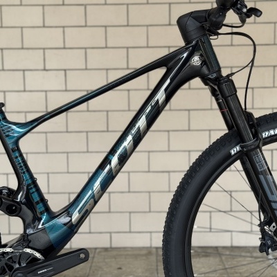 Bicicleta de montanha com quadro carbono preto e azul, pneus pretos e suspensão dianteira