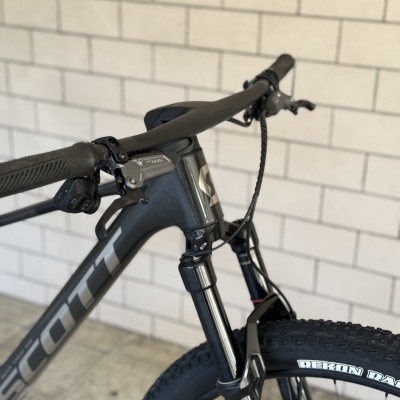 Bicicleta de montanha preta com suspensão RockShox e pneus PREKON DAK contra parede de azulejos brancos