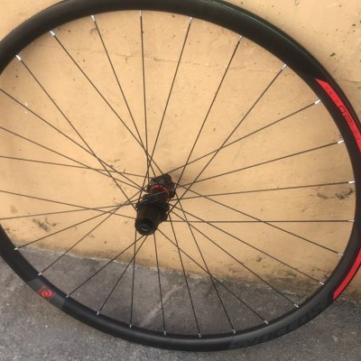 Roda de bicicleta preta com detalhes vermelhos e verdes encostada numa parede bege.