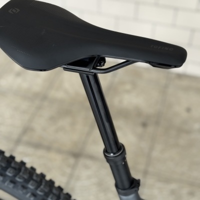 Selim de bicicleta preto montado numa coluna de selim preta e pneu rugoso ao fundo