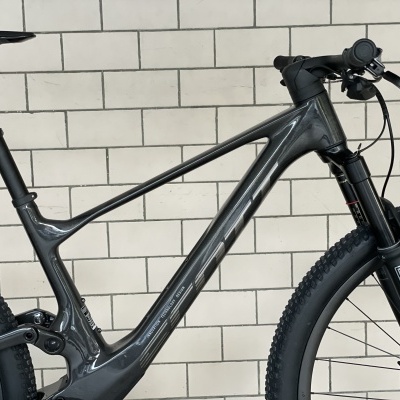 Bicicleta de montanha com quadro cinzento e pneus pretos junto a uma parede branca