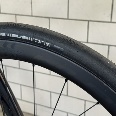Pneu de bicicleta preto com inscrições brancas e aro preto junto a parede de azulejos