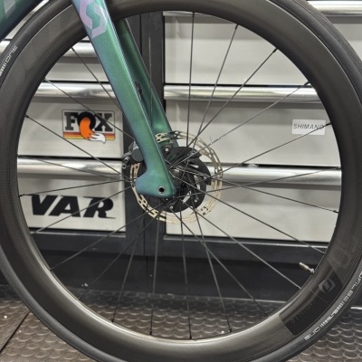 Roda dianteira de bicicleta com aro preto e garfo verde metálico.