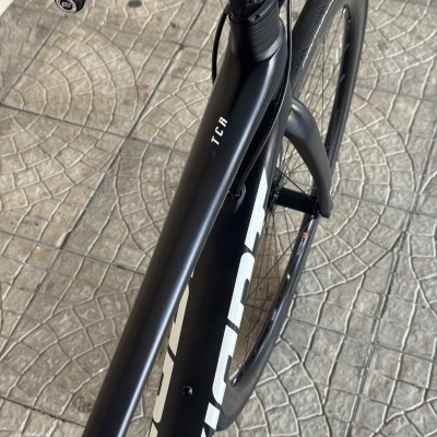 Bicicleta preta de estrada com inscrição TCR no quadro sobre piso de pedra.