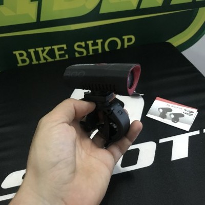 Luz traseira para bicicleta preta e vermelha segurada por uma mão, com fundo de loja de bicicletas